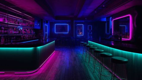 Neon Lounge Bar with Cyan Magenta LED Counters Reflecting on Wooden Floor
