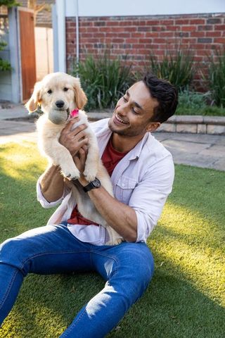 Happy man enjoying playtime with golden retriever puppy in sunlit backyard