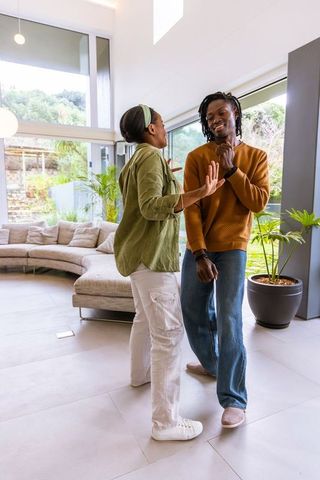 African american couple laughing and gesturing in sunlit open-plan living room with curved sofa