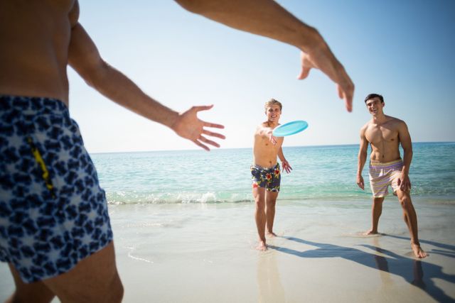 Shirtless male friends playing frisbee on shore at beach