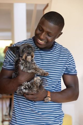 Man in blue striped shirt holding dog at home