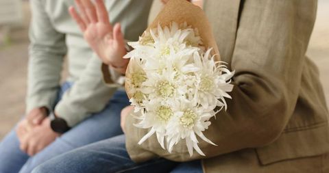 Senior couple sitting on bench with white chrysanthemum bouquet being declined