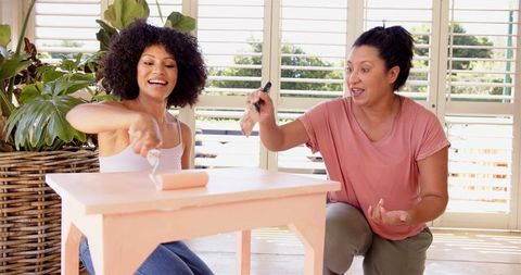Mother and adult daughter painting table engaged in diy home project