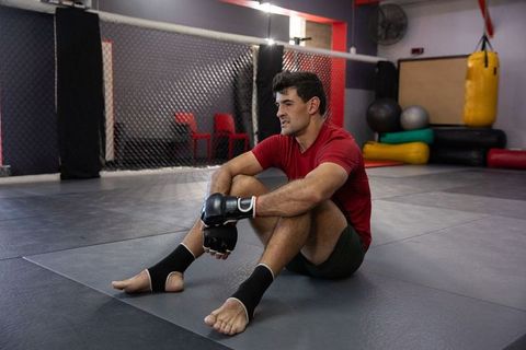 Mma fighter sitting on mats after workout showing focus, determination, recovery