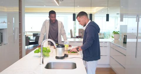 Diverse friends chopping vegetables on modern marble kitchen island with blender