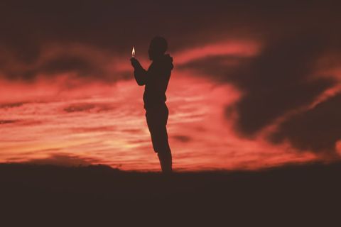 Silhouette of Person Holding Candle Against Dramatic Sunset