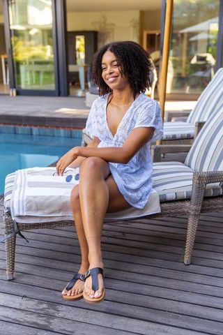 African american woman lounging by pool in blue cover-up smiling on sunny patio relaxation