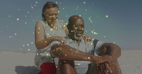 Senior couple relaxing on sunlit beach with golden sparkles, affectionate seaside moment
