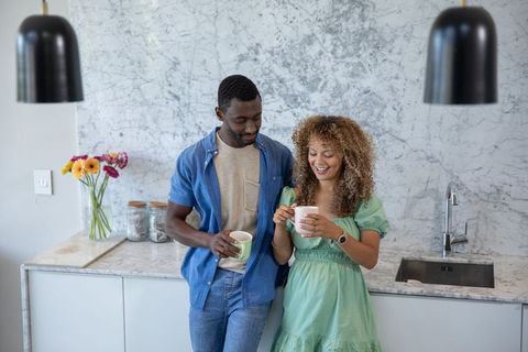 Diverse couple enjoying coffee in modern marble kitchen sharing relaxed morning conversation