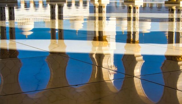 Reflecting ornate arches and gold capitals on marble floor showing geometric symmetry