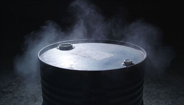 Industrial steel drum releasing vapor under moody overhead rimlit light with smoke