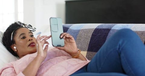 African American Woman Relaxing on Couch with Smartphone and Earbuds