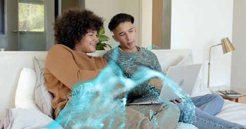 Young men collaborating on laptop with holographic data wave on cozy couch