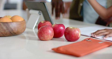 African american couple writing notes at kitchen counter with apples and tablet