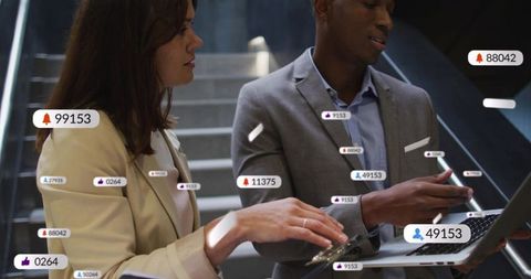 Colleagues collaborating over laptop showing social media notification overlays on office stairs