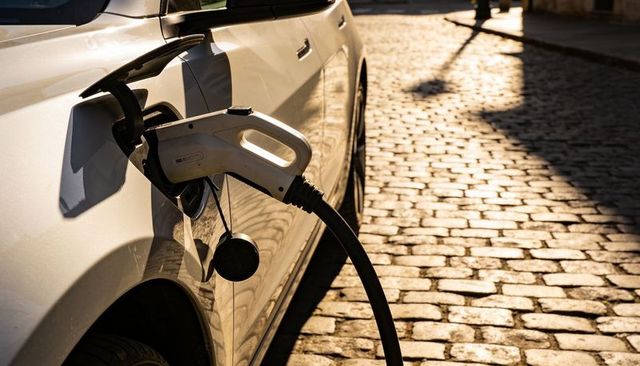 White electric car charging on sunlit cobblestone street during golden hour