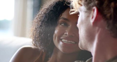 Couple sharing intimate moment on couch smiling woman leaning toward partner backlit by window