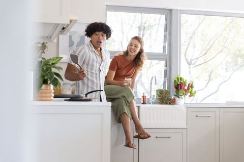 Young couple cooking together in bright kitchen, man flipping pan while woman laughing
