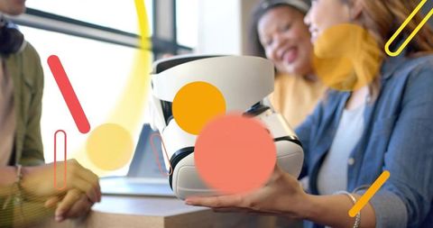 Creative team sharing white vr headset and laptop in sunlit coworking space with colorful overlays