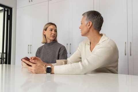 Senior woman and middle-aged daughter talking over smartphone at minimalist kitchen island