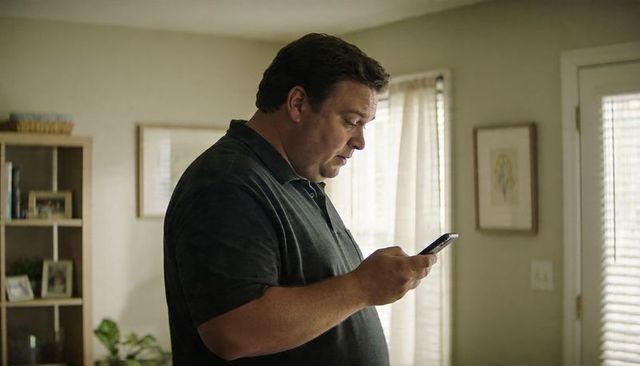 Middle-aged man checking smartphone in sunlit living room, casual home lifestyle moment