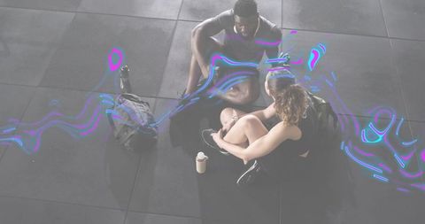 Overhead gym partners sitting and adjusting shoes with neon swirl for fitness recovery