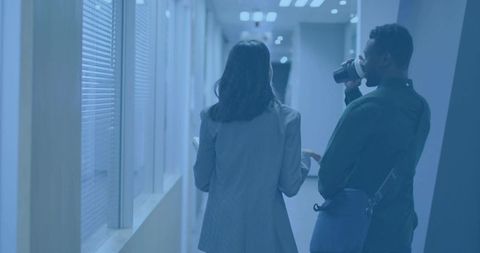 Colleagues walking and talking in modern office corridor holding tablet and coffee cup