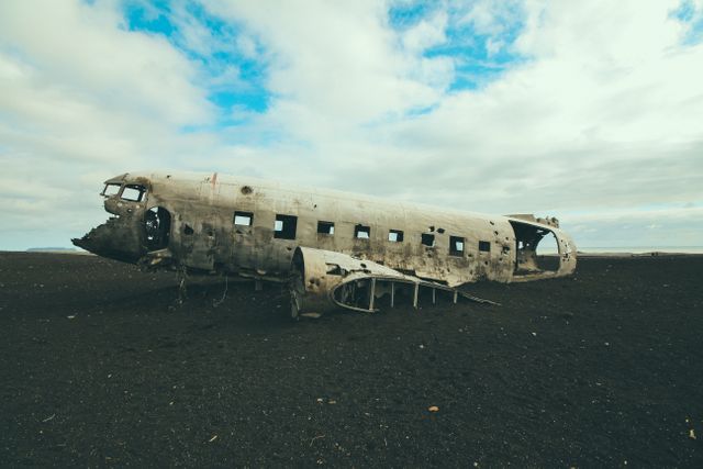 Photo depicts an abandoned plane wreckage on a black sand beach in Iceland, under a dramatic cloudy sky. Useful for travel blogs, articles about Iceland, aviation history, themes of solitude and decay, or promotional materials for Nordic tours.