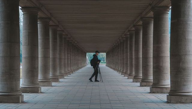 Photographer Adjusting Camera on Tripod in Symmetrical Stone Colonnade