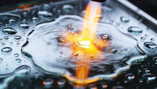 Flame Tip Striking Water Creating Crown Splash on Glossy Glass with Sparks and Droplets