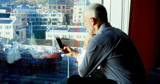 Mature Businessman Contemplating Through Office Window with Smartphone - Download Free Stock Images Pikwizard.com