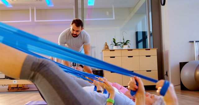 Personal trainer assisting senior women in a gym while they exercise with resistance bands. Perfect for promoting senior fitness classes, physical therapy programs, healthy living for seniors, and group exercise sessions.