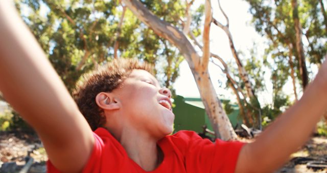 Young boy enjoying a sunny day outdoors, arms outstretched in joy. Perfect for concepts on childhood, happiness, freedom, and outdoor activities. Use in advertisements, parenting articles, or any materials highlighting children's well-being and enjoyment.