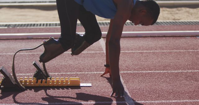 Paralympic athlete with prosthetic legs preparing at starting blocks for sprinting on track. Useful for promoting sports inclusivity, disability awareness, athletics competition events, fitness motivation, and training programs.