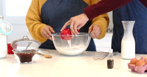 Couple baking together pouring milk into glass mixing bowl in sunlit modern kitchen