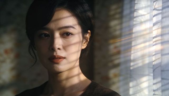 Moody portrait of asian woman with blinds shadows and warm window light, contemplative