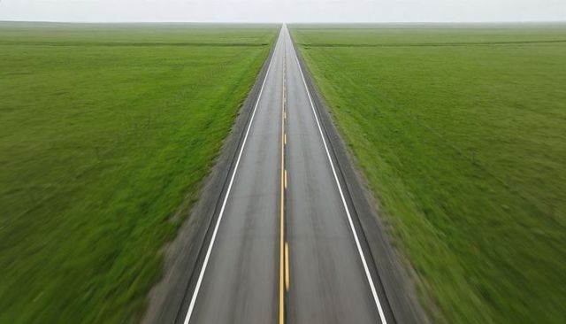 Stretching straight highway running toward horizon through vast green prairie