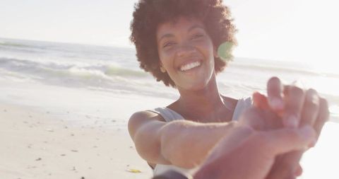 Smiling Black woman holding hand on sunlit beach enjoying joyful connection and freedom
