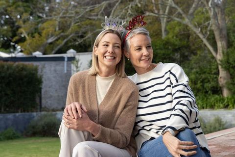 Two women celebrating christmas in cozy backyard with festive headbands and warm knitwear