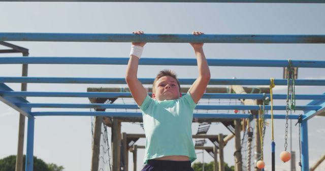 A boy in a light blue t-shirt and dark shorts is playing on monkey bars at an outdoor playground. His focused and determined expression suggests he is enjoying an adventurous, active, and healthy playtime. This is a perfect image for topics related to childhood, physical activity, outdoor fun, and kids fitness.