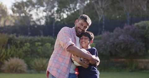 Happy Father Hugging Son Holding Soccer Ball on Sunny Lawn