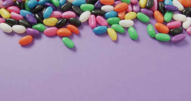 Various brightly colored jelly beans are scattered across a purple background. Perfect for use in advertising, marketing materials, and social media to convey fun, childhood memories, or promote confectionary products. Useful as a colorful backdrop for party invitations or festive decorations, especially for occasions like Easter or children's parties.