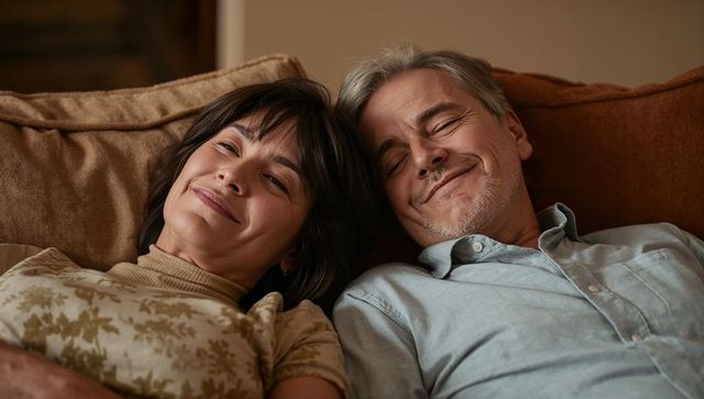 Mature couple relaxing on cozy sofa sharing intimate smile, warm indoor lifestyle