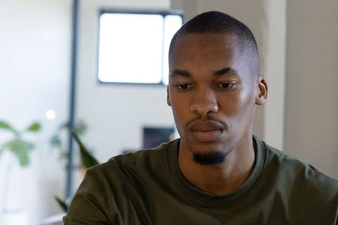 African-american man contemplating by window with indoor plant and soft natural light