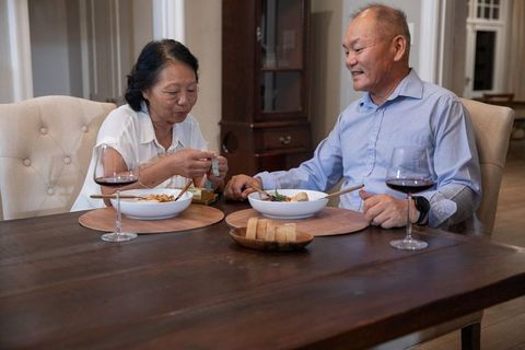 Senior chinese couple sharing cozy dinner with wine and chopsticks at home