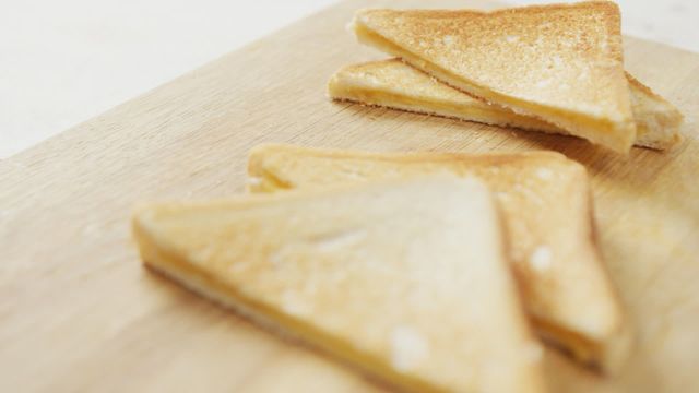 Slices of toasted cheese white bread sandwiches placed on a wooden chopping board. Ideal for illustrating breakfast recipes, snack ideas, or quick meal preparations. Could be used in blogs, menus, and food-related advertisements.