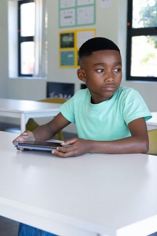 African american schoolboy using tablet in classroom, looking thoughtful and distracted