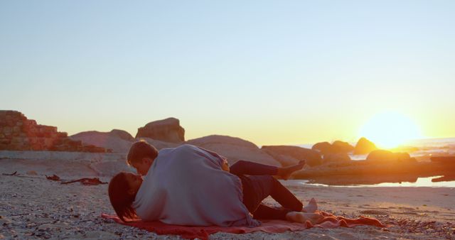 A couple enjoys a romantic moment lying together on a beach at sunset, with copy space. Their affectionate pose captures the beauty and tranquility of a seaside evening.