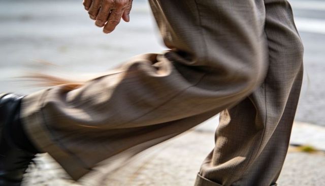 Senior hurrying across crosswalk in brown trousers with motion-blurred stride