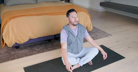 Mature man meditating on yoga mat in calm bedroom